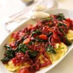 A platter of ravioli topped with healthy sautéed veggies.