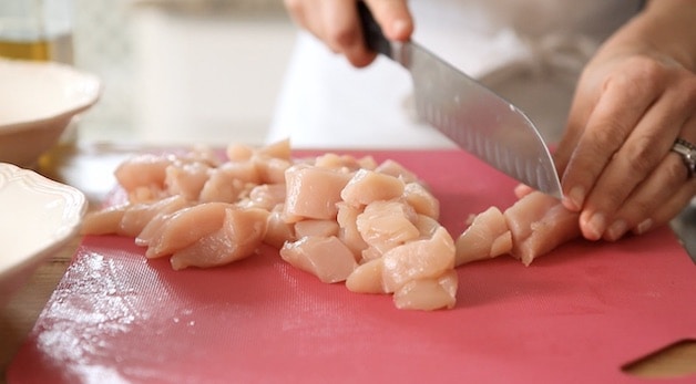 Slicing chicken tenderloin on a red cutting board