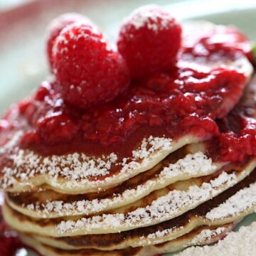 A stack of lemon ricotta pancakes with a raspberry sauce topping