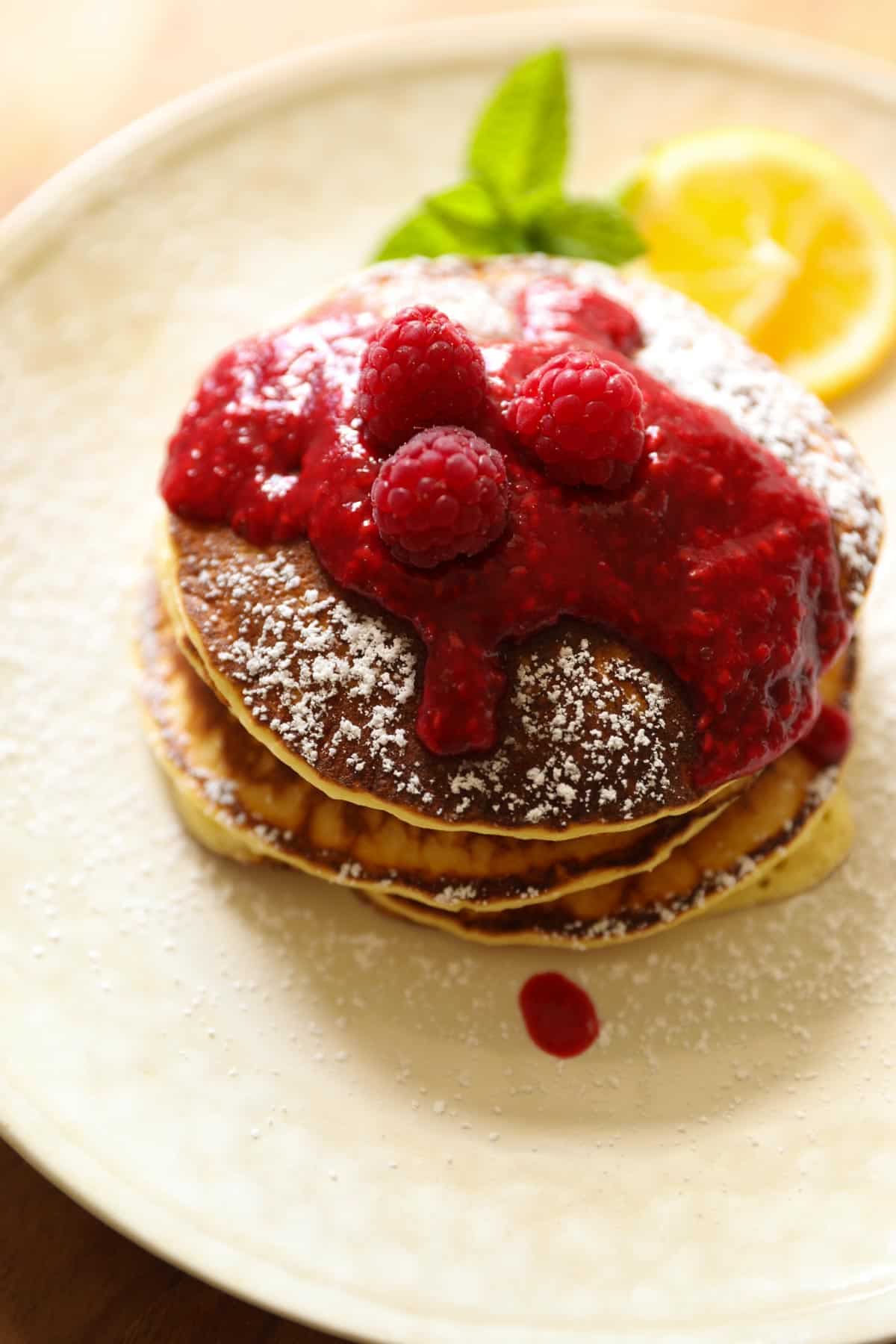 A stack of lemon ricotta pancakes with raspberry sauce