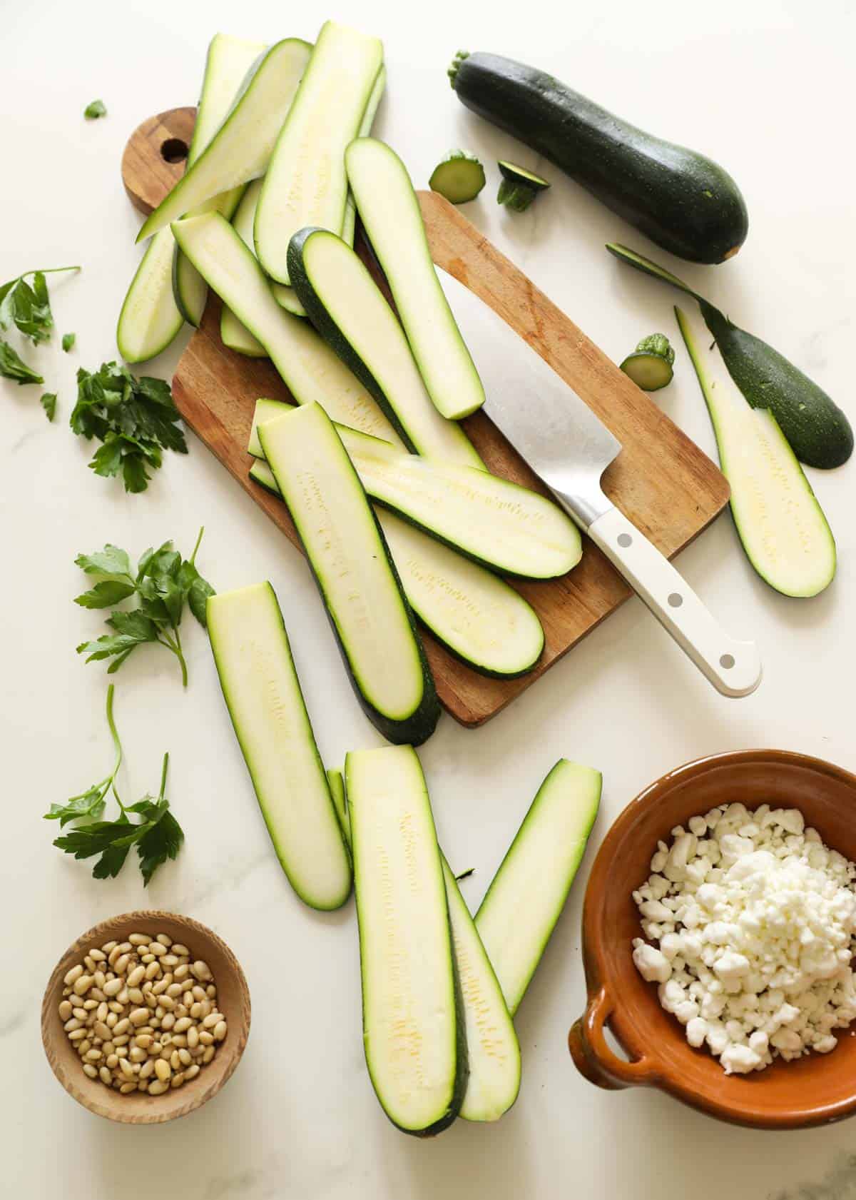 Sliced zucchini on a cutting board with goat cheese and pine nuts