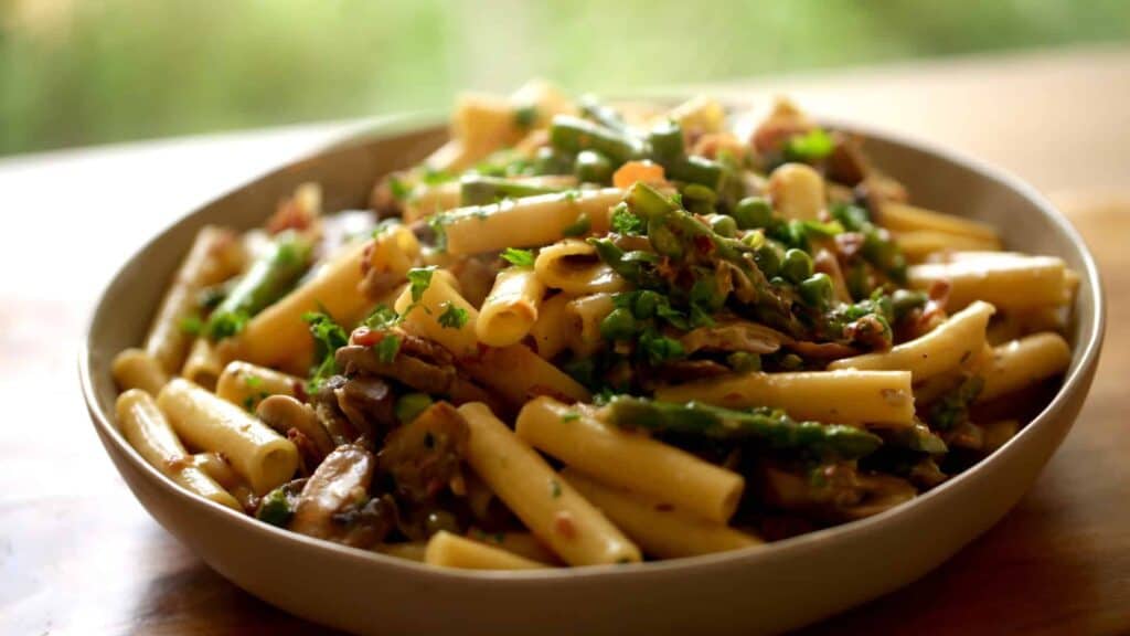 Large platter of pasta with fresh parsley, peas asparagus and proscuitto