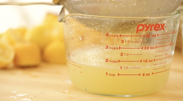 Straining lemon juice into a large Pyrex pitcher