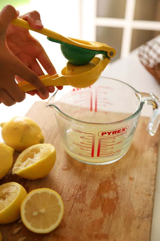 Squeezing Lemons into a pyrex pitcher with a lemon squeezer.