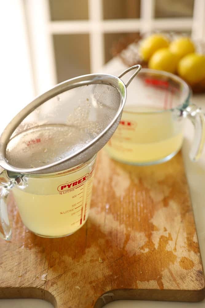 Straining Lemon juice through a strainer into a measuring cup.
