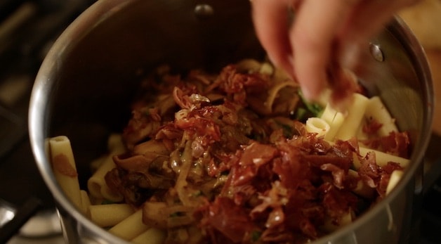 placing crispy cooked prosciutto in a pot of pasta