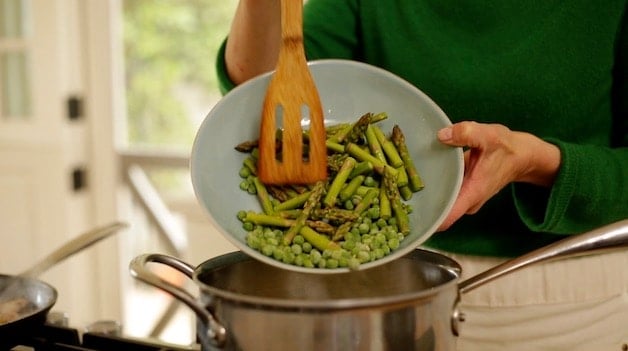 adding frozen peas and fresh asparagus to a pot of boiling water with pasta