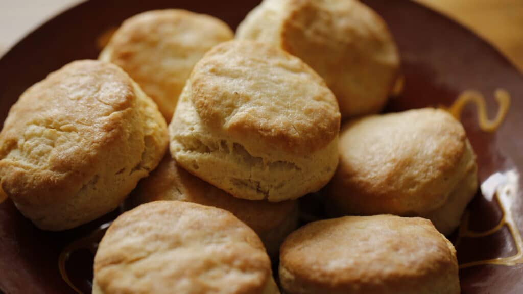 A mound of flakey buttermilk biscuits on a terra cotta plate