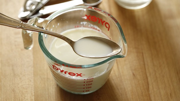 Pyrex Pitcher with a spoon of milk over a pitcher filled with milk 