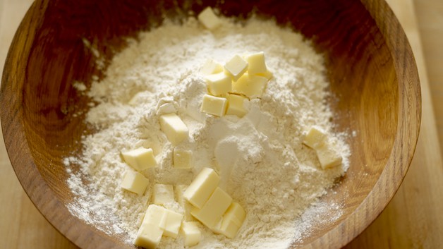 Flour and dry ingredients in a wooden bowl with diced butter on top