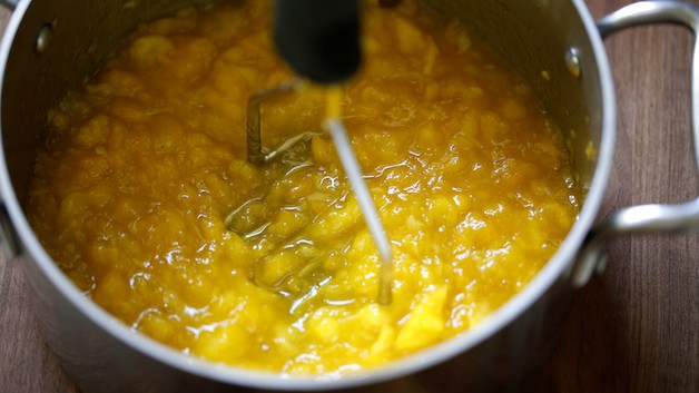 mashing mangoes in a pot with a potato masher