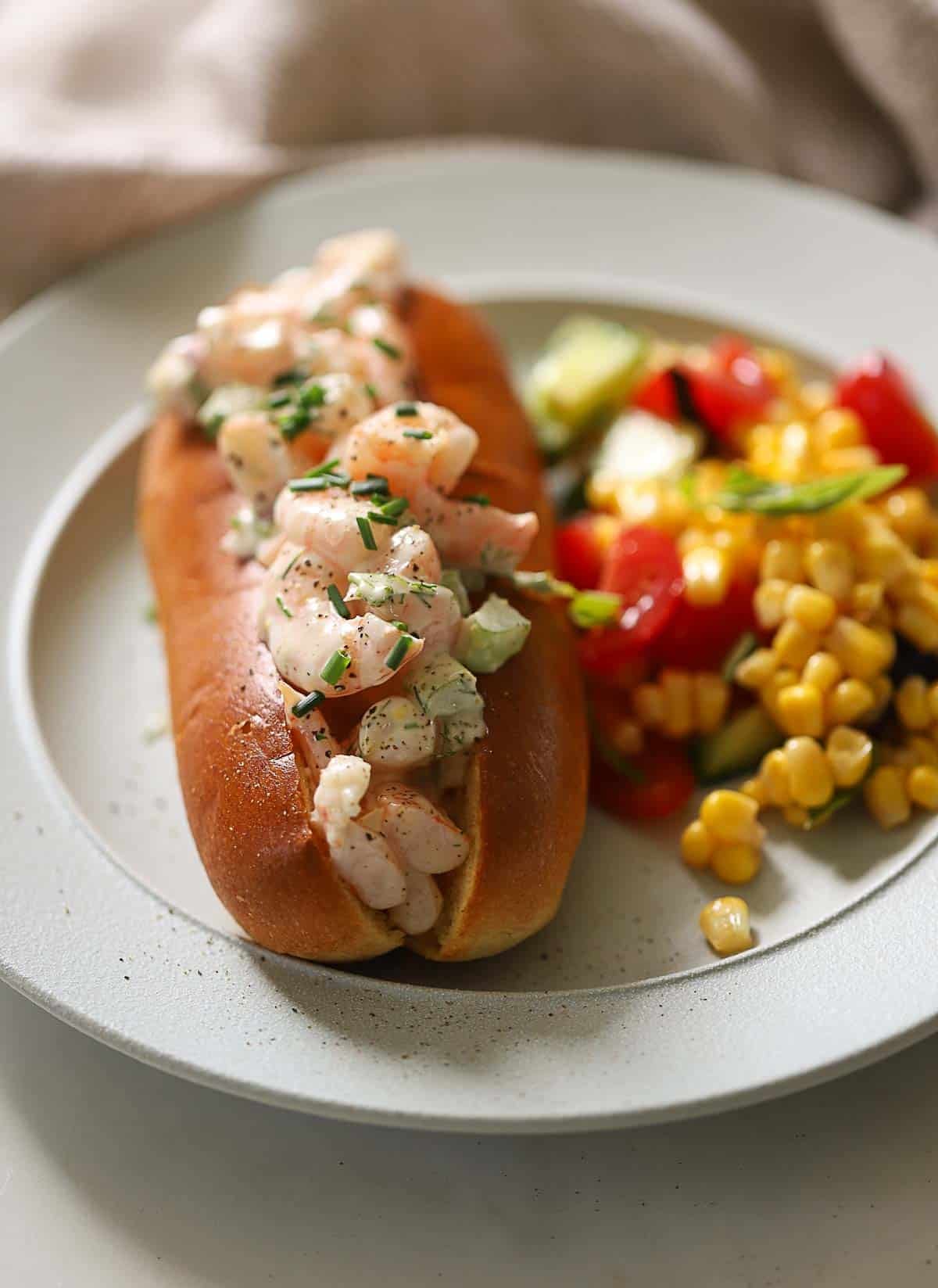 a New England Style Shrimp Roll on a plate with a spoonful of corn salad.