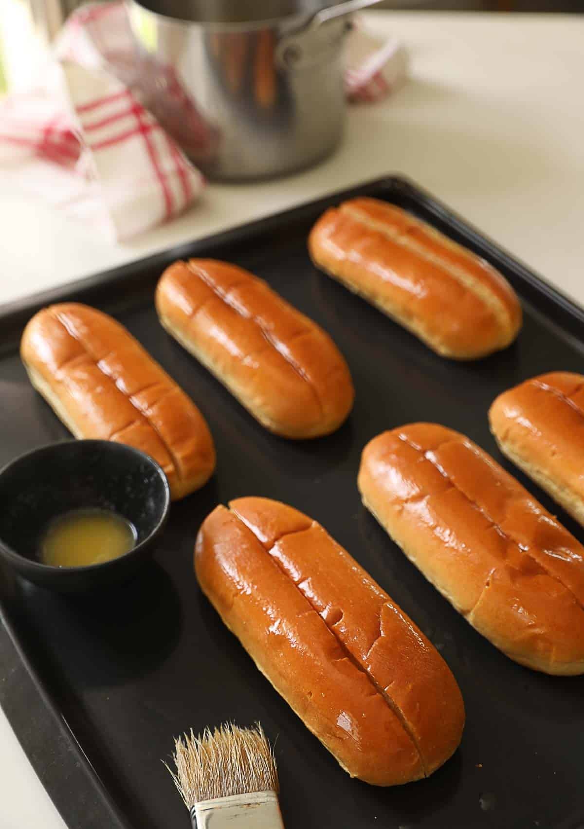 Split Top Buns being buttered on a baking sheet.