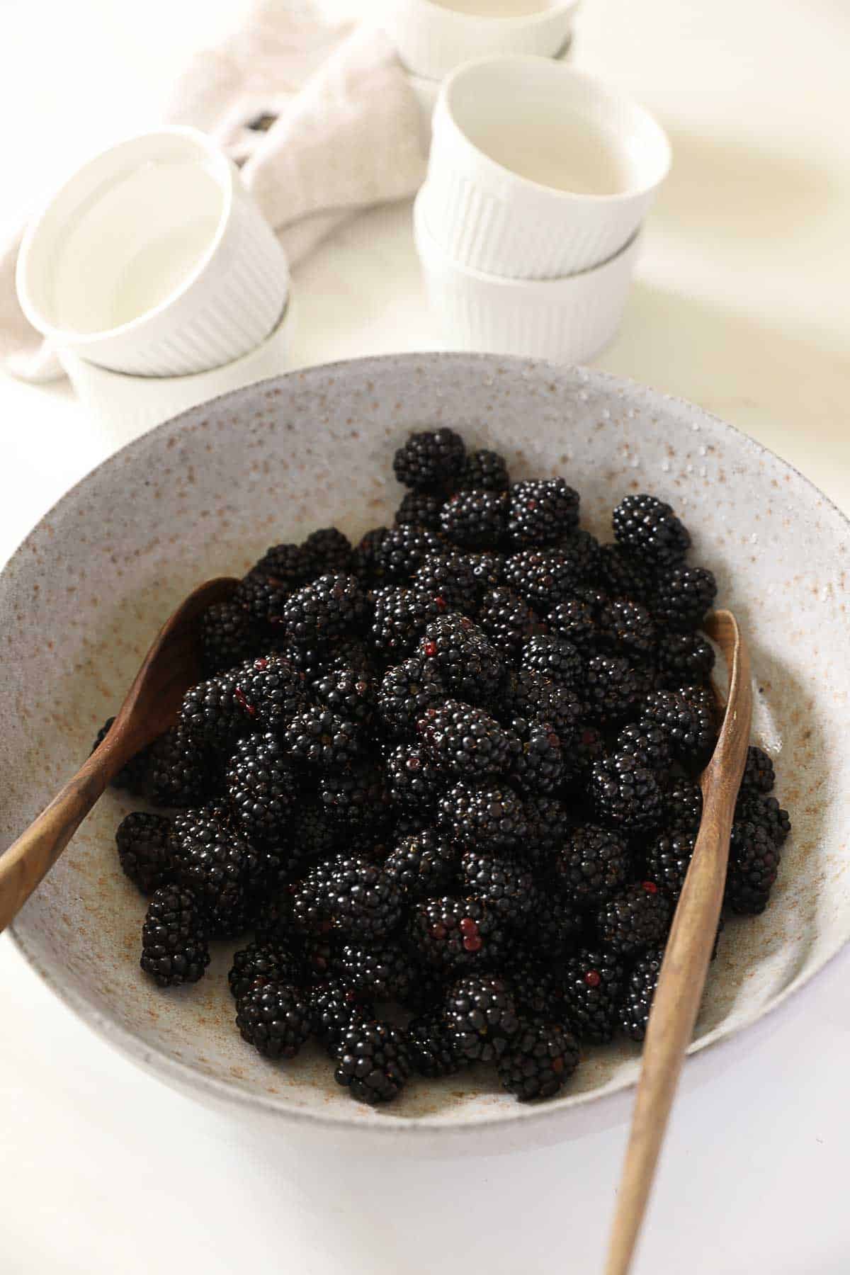 Blackberries in a bowl with wooden spoons.