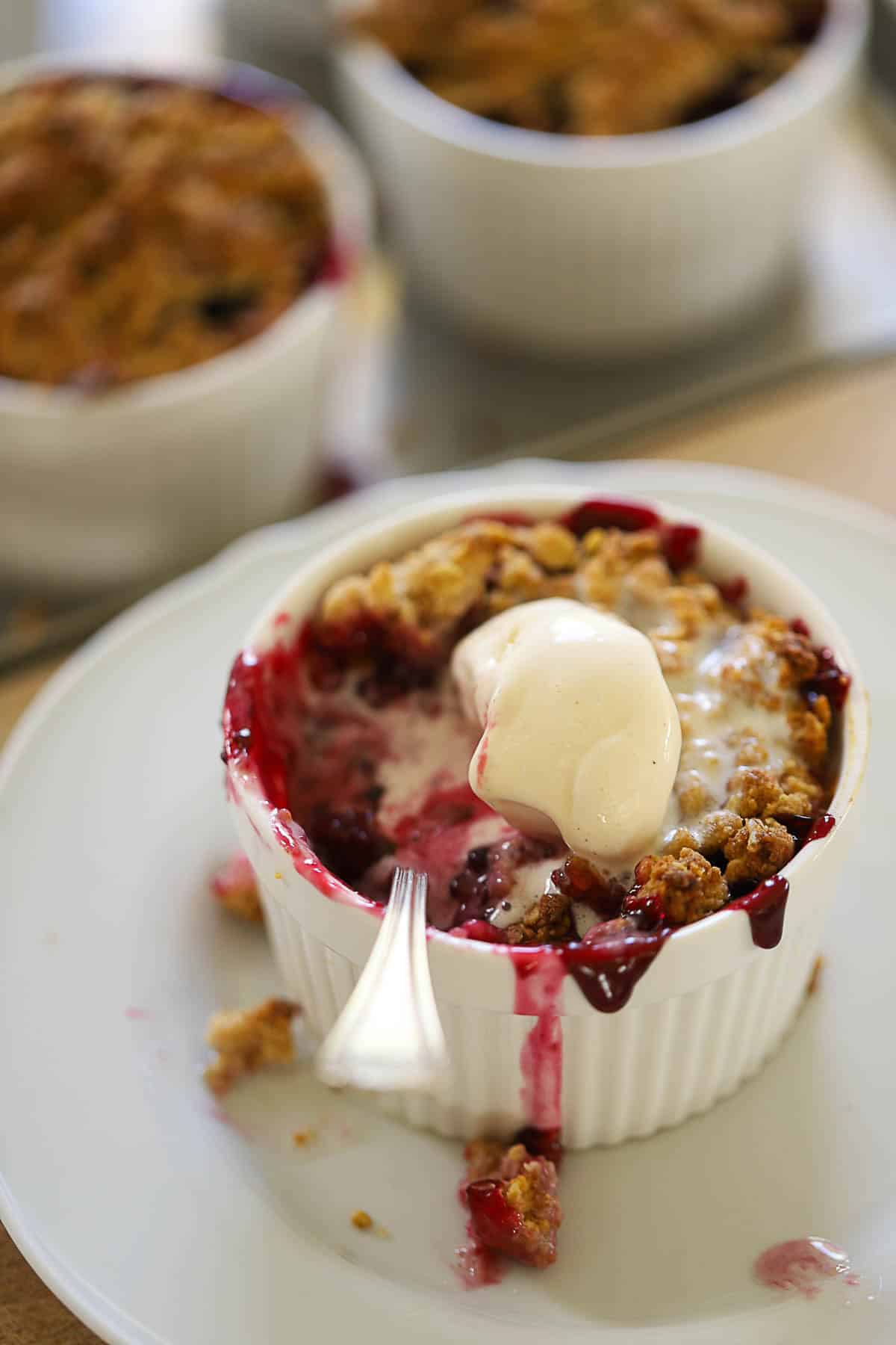 A ramekin of blackberry crisp with melting ice cream.