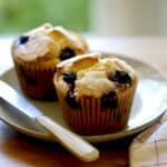 A vertical image of Blueberry Muffins on a plate with a knife