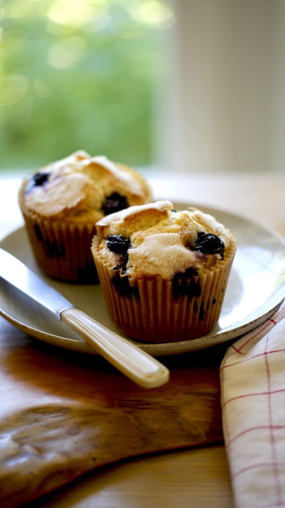 A vertical image of Blueberry Muffins on a plate with a knife
