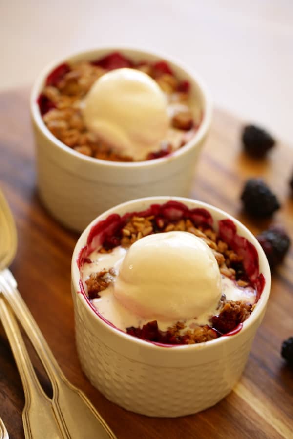 Two blackbery crumbles with ice cream melting on a cutting board