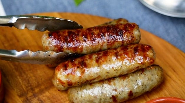 a tong placing grilled sausages on a serving board