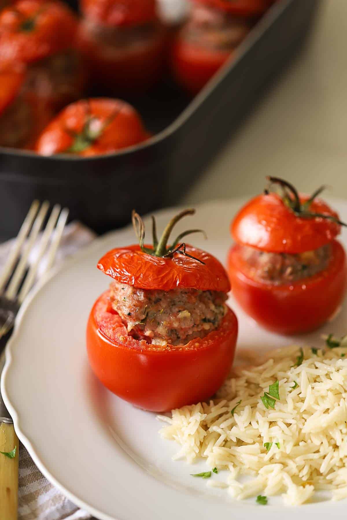 Two baked stuffed tomatoes on a plate with rice.