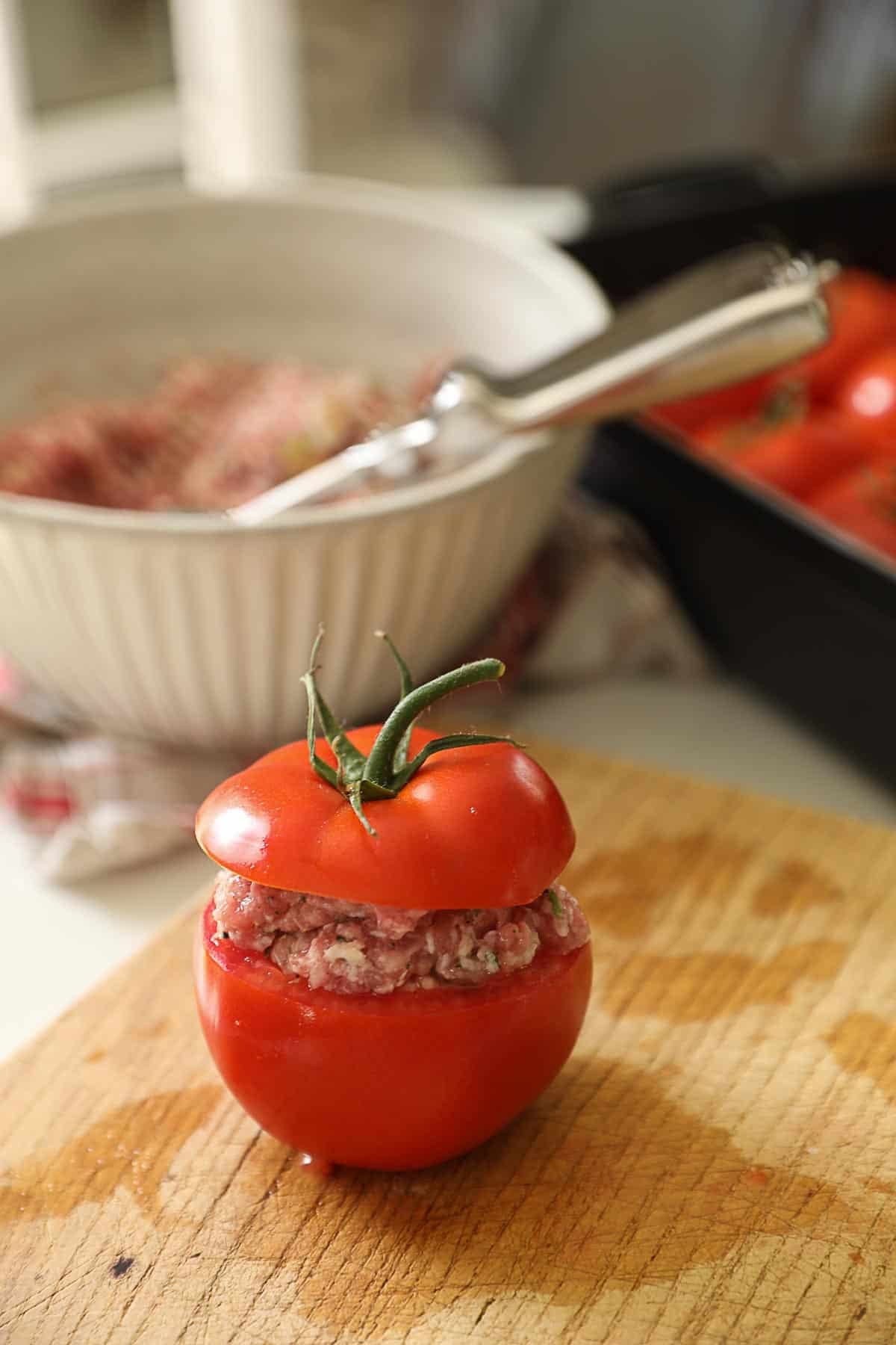 a tomato on a cutting board stuffed with meat mixture.