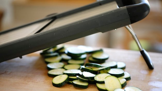 Sliced zucchini rounds on a cutting board with a mandoline