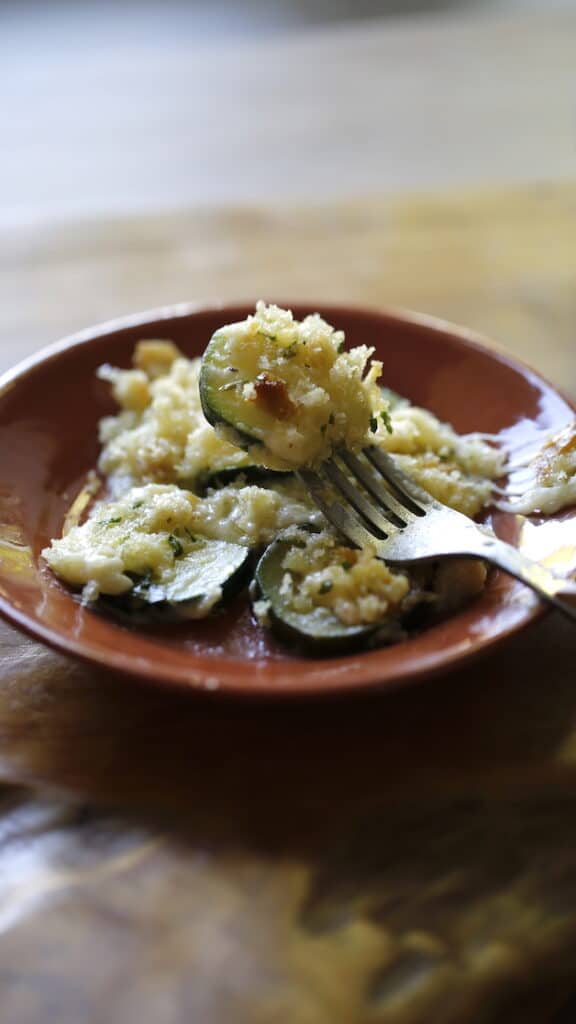 a terra cotta plate with a fork with a piece of zucchini gratin