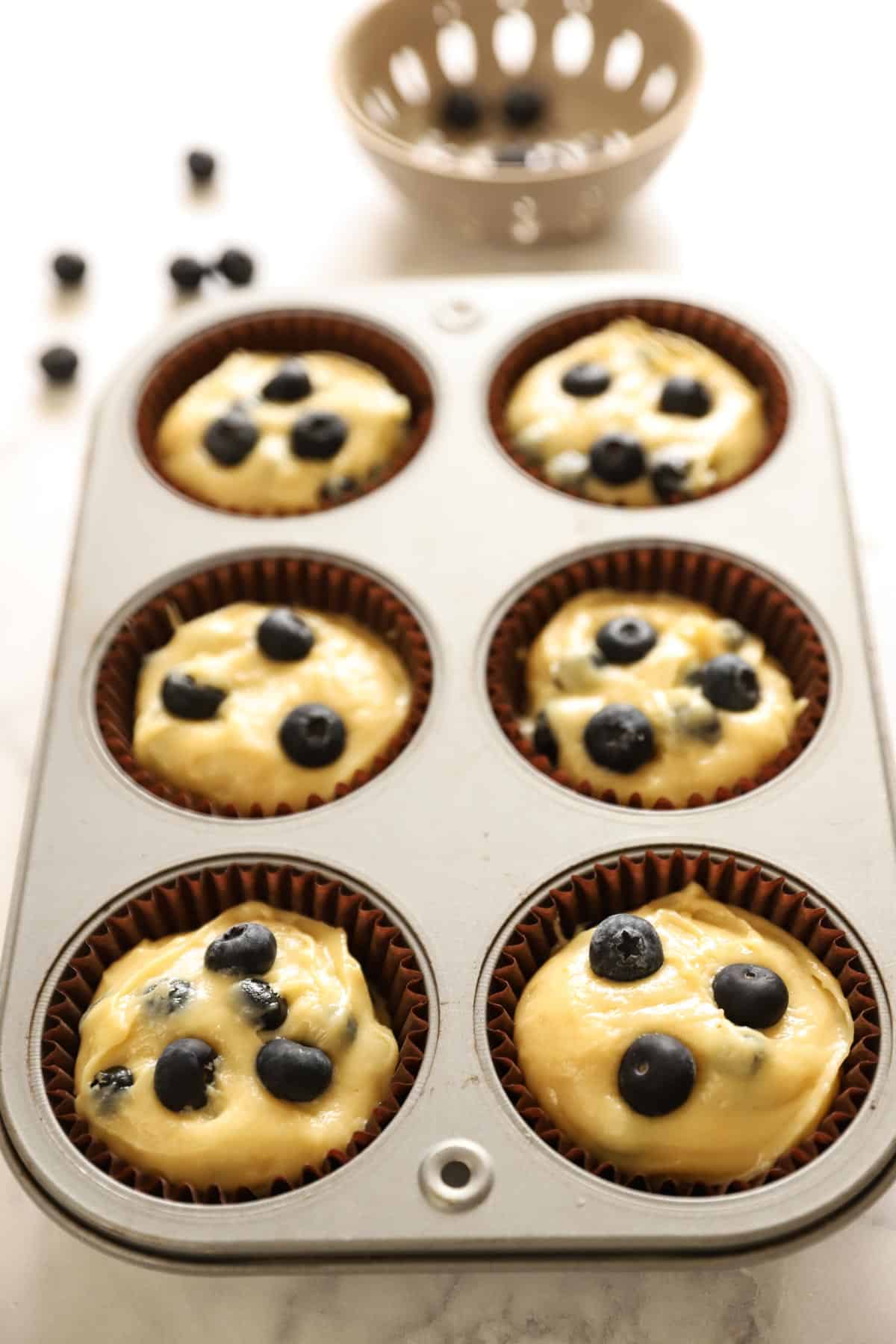 muffin batter filled in a muffin tin, topped with fresh blueberries