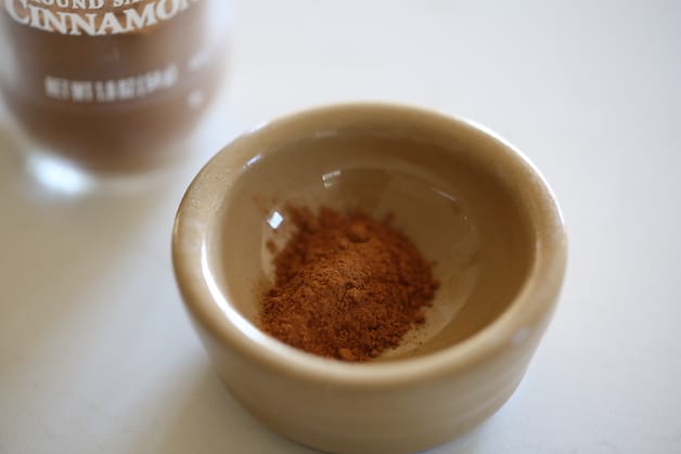 ground cinnamon in a brown little bowl with cinnamon jar behind it