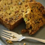 A slice of zucchini bread with crumbs on a plate with a fork.