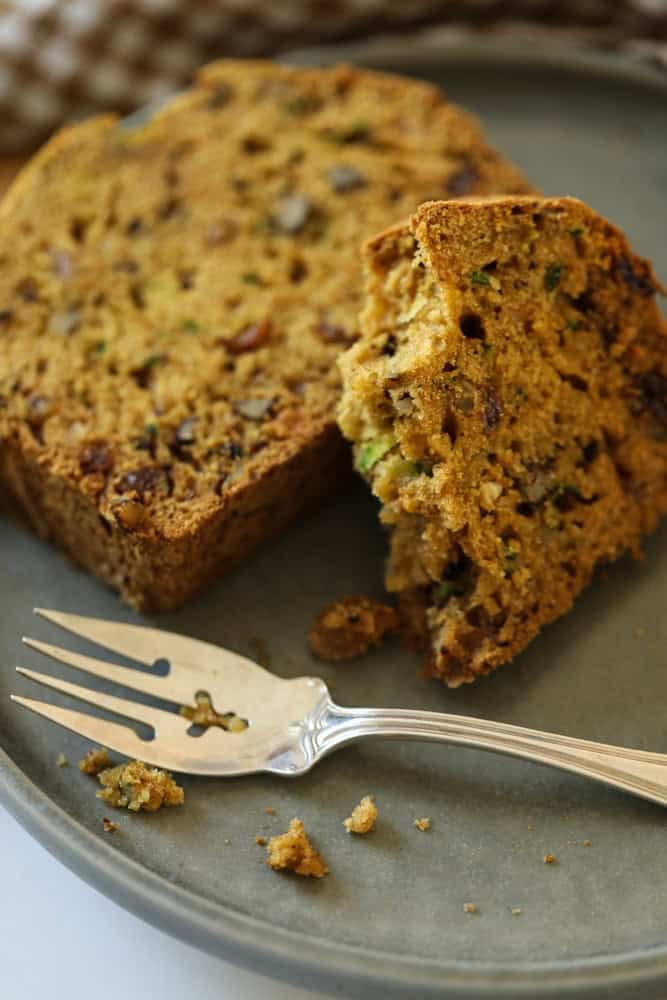 A slice of zucchini bread with crumbs on a plate with a fork.