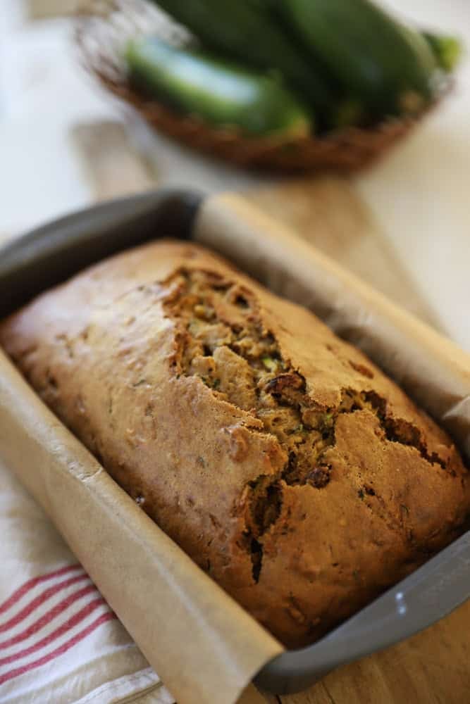 a loaf pan lined with parchment paper and a fully baked zucchini bread.