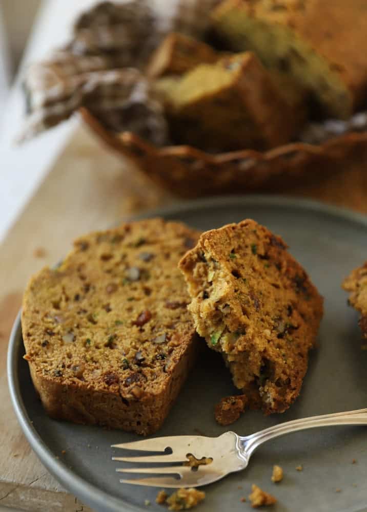 Two slices of Zucchini Bread on a plate with a basket in the distance