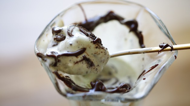 a spoon in an ice cream glass taking a bite of mint chip ice cream with hot fudge sauce