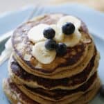 a vertical image of a blue plate piled high with Oat Floiur Pancakes with Bananas and Blueberries on top