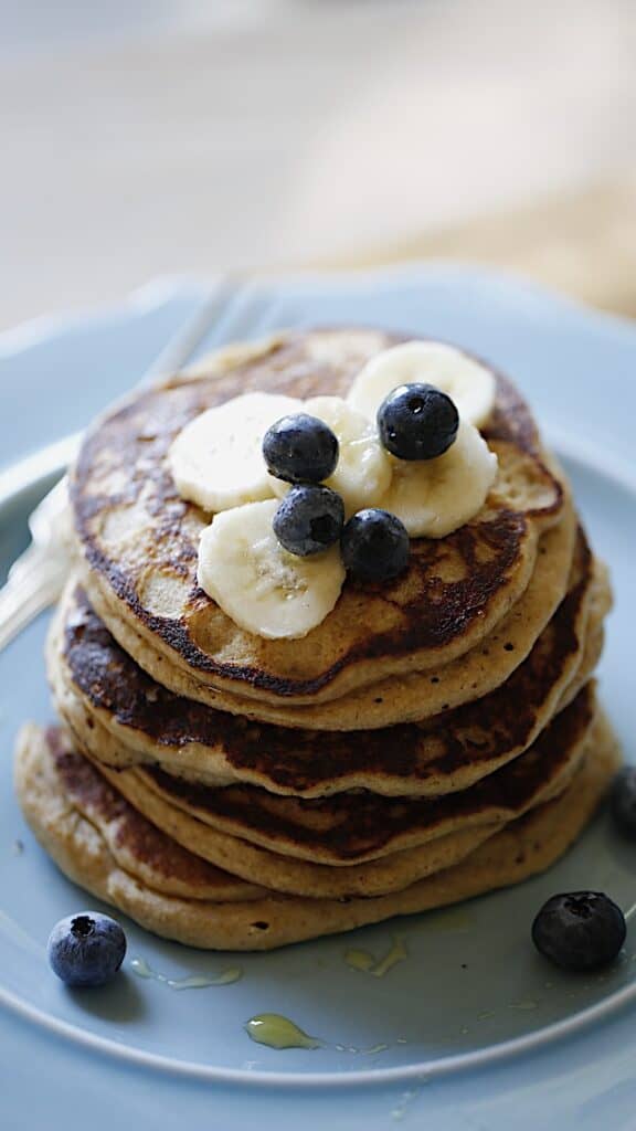 a vertical image of a blue plate piled high with Oat Floiur Pancakes with Bananas and Blueberries on top