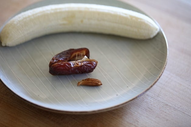 a peeled banana and a split open date with pit on a plate