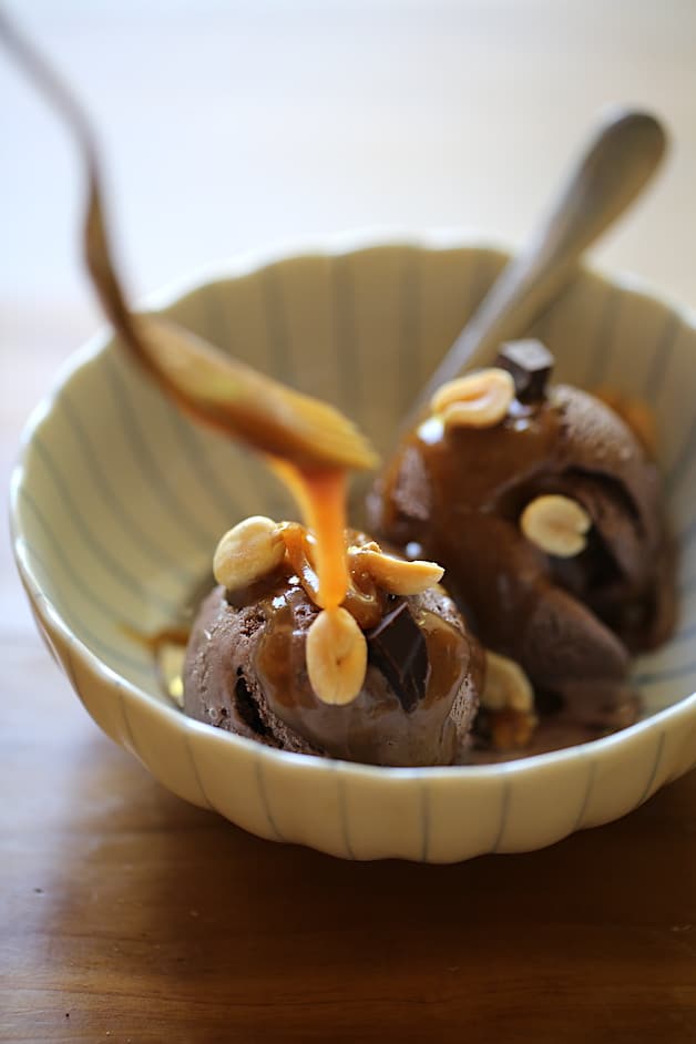 drizzling peanut butter sauce on chocolate ice cream in a bowl with peanuts and chocolate chunks