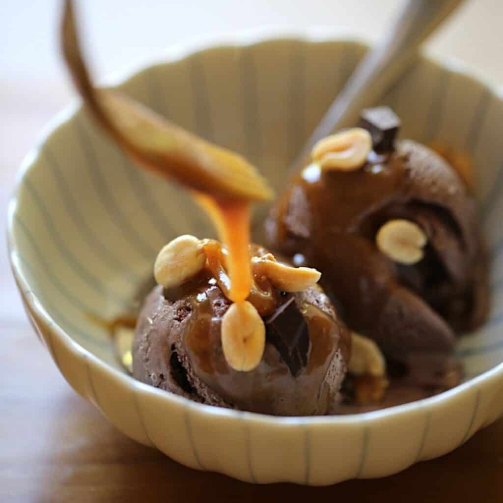 a fork drizzling peanut butter sauce on to chocolate ice cream garnished with peanuts