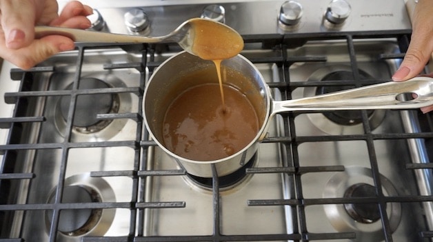 a spoon drizzling peanut butter ice cream sauce from a sauce pot on a cooktop