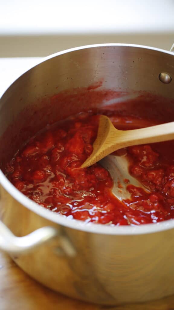 a vertical image of chunky strawberry sauce with a wooden spoon