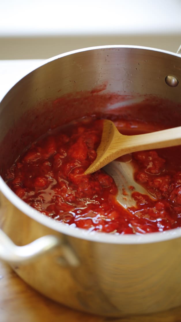 a vertical image of chunky strawberry sauce with a wooden spoon