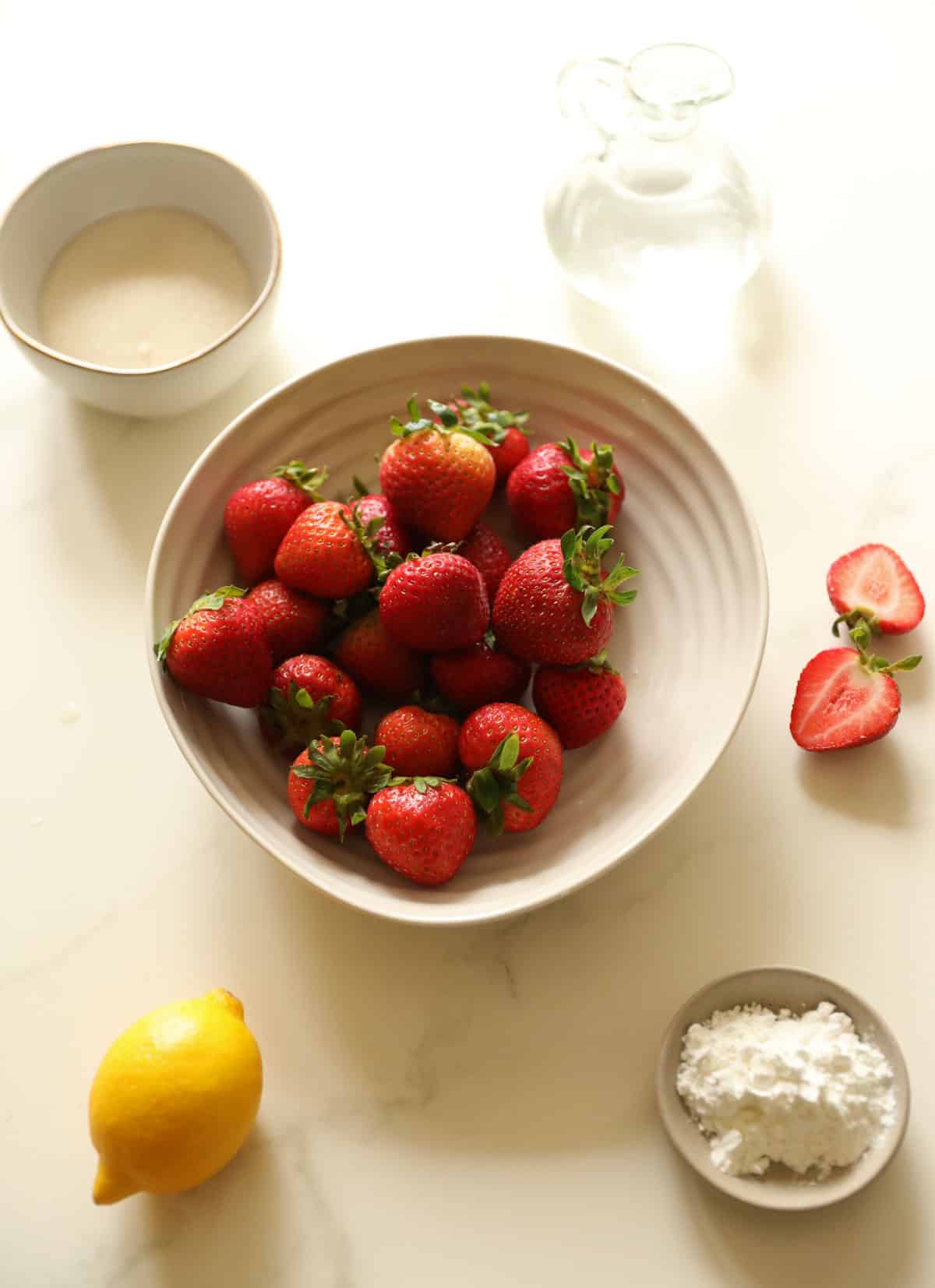 Strawberries, lemon, water, sugar and cornstarch laid out on a counter