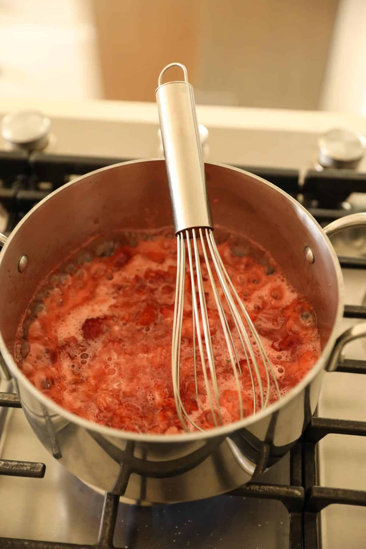 a simmering strawberry sauce with a wire whisk in the pot