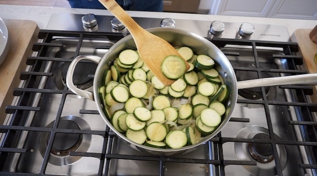 a wooden spatula showing a zucchini round over a skillet that has been cooked 