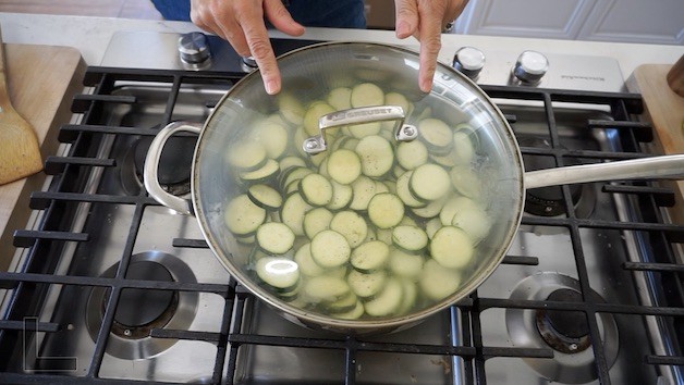 Sliced zucchini steaming in a skillet with a glass cover