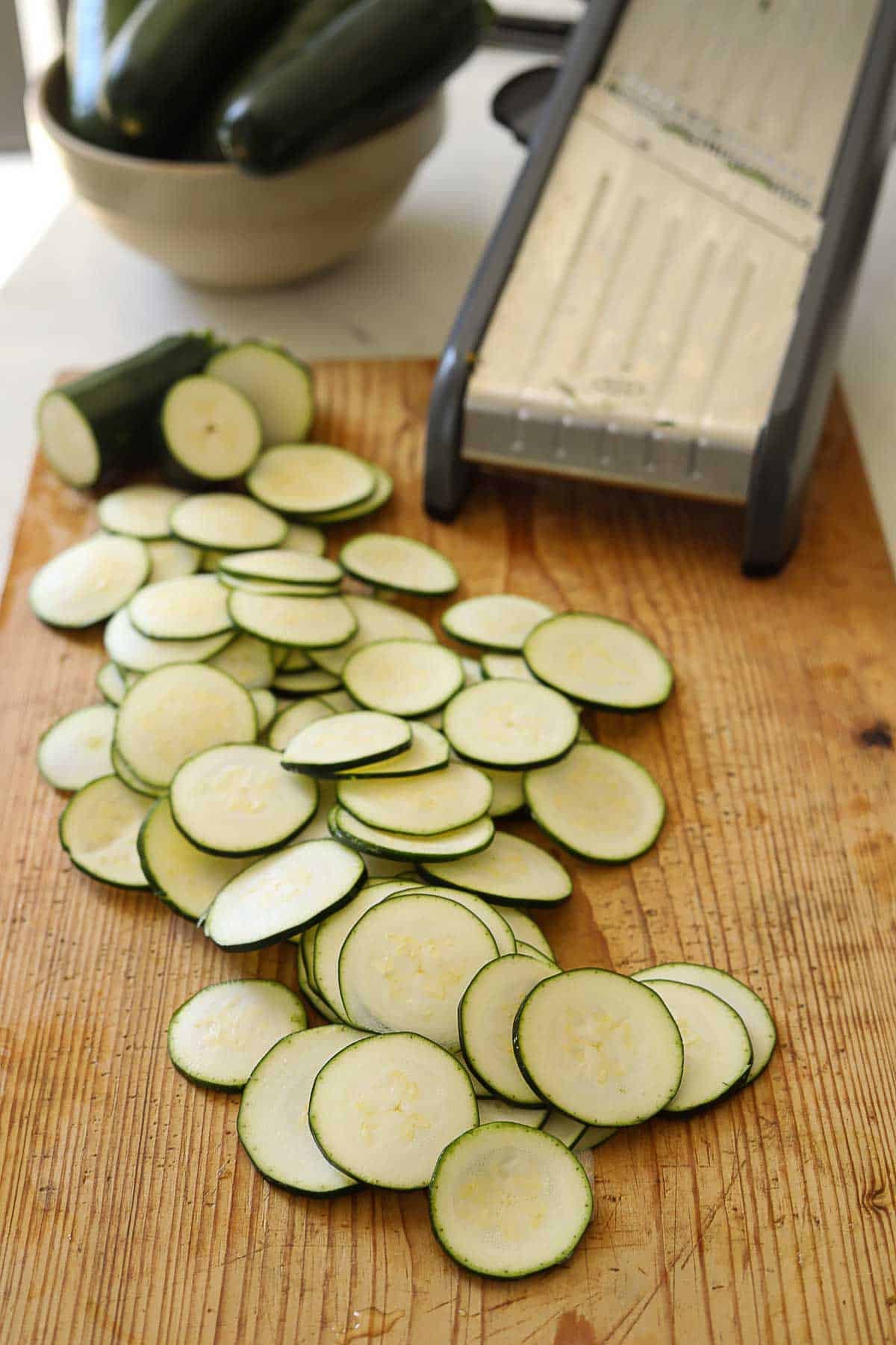 1/8" rounds of zucchini being sliced with a mandoline.