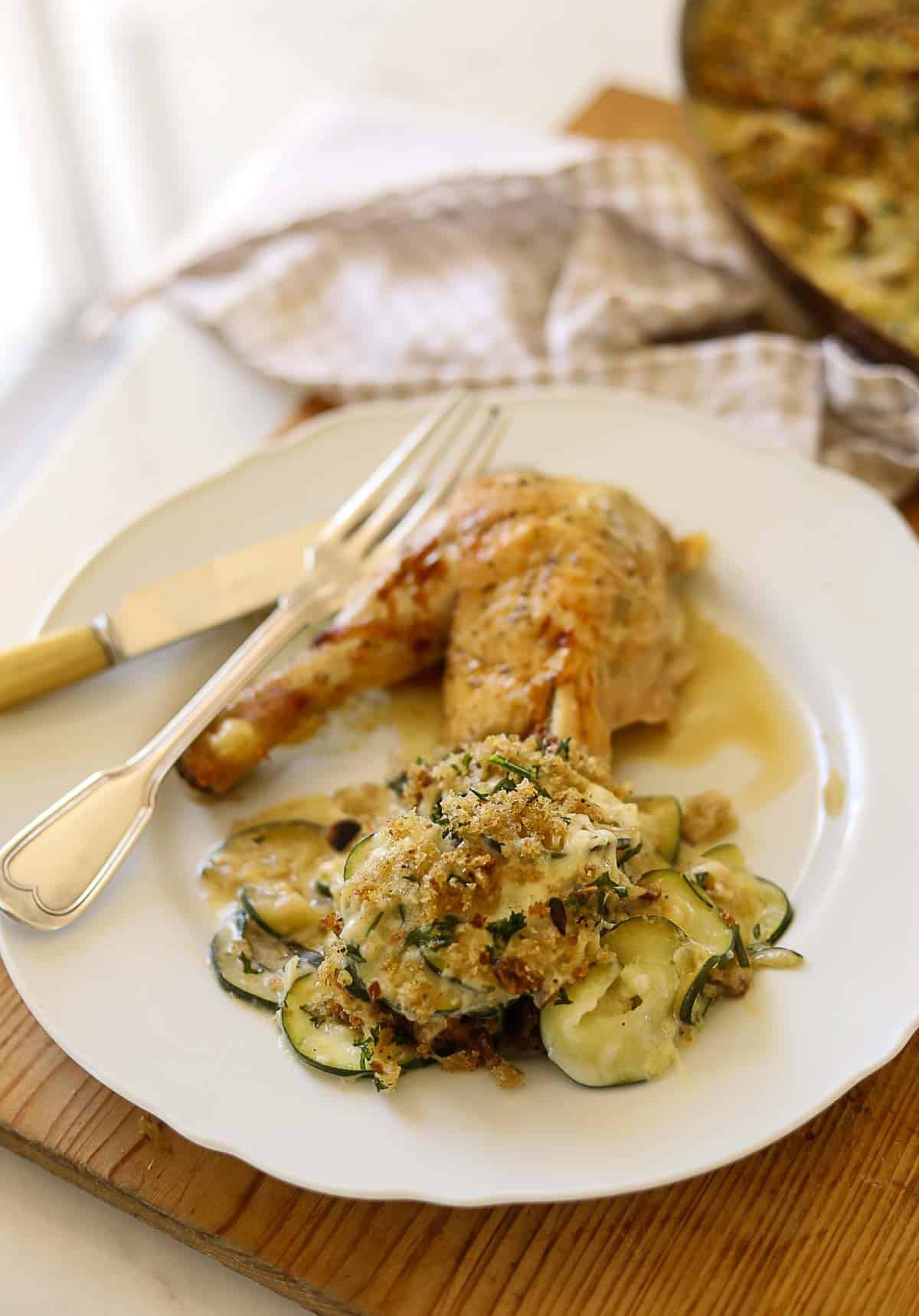 A roast chicken leg with a side dish of zucchini gratin.