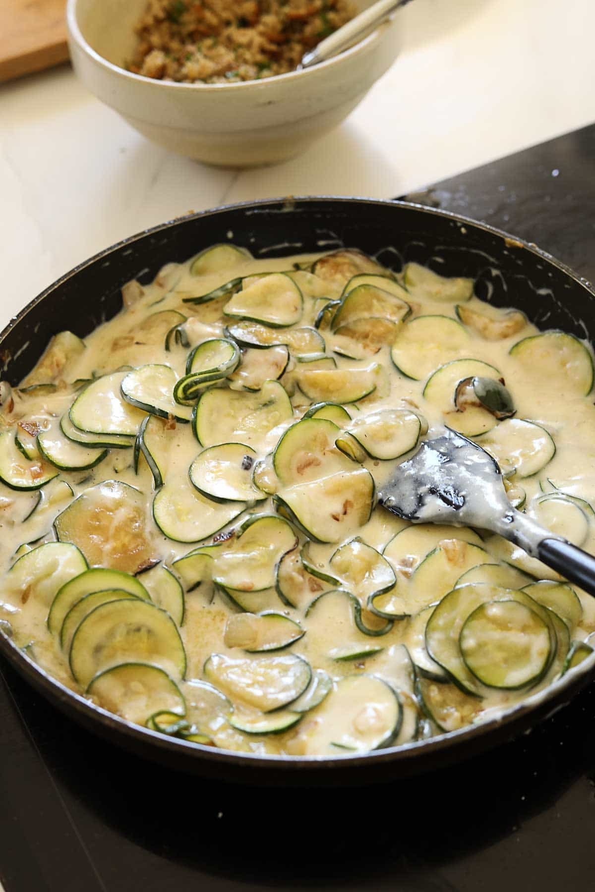 zucchini and onion tossed in bechamel sauce in a skillet.