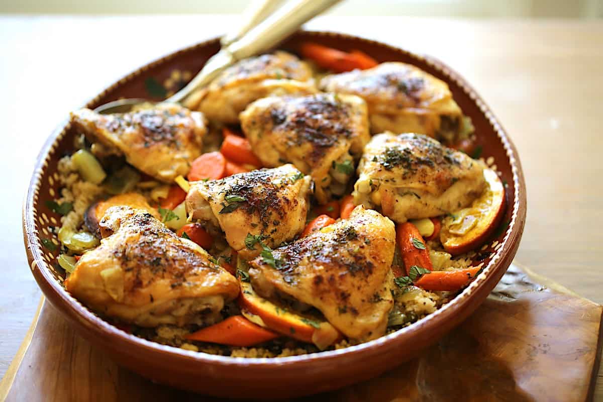 sheet pan chicken thighs on top of a platter of couscous and vegetables